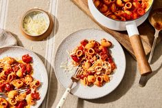 two plates of pasta with sauce and cheese next to a bowl of grated parmesan cheese