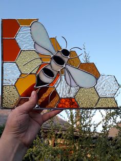 a hand holding up a stained glass window with a bee on it's side