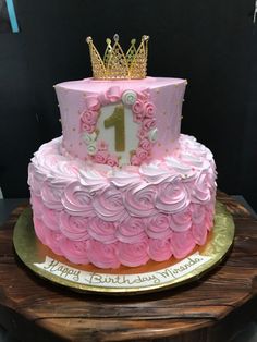 a pink and gold birthday cake with a number one on the top is sitting on a wooden platter