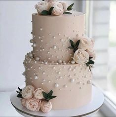 a three tiered pink wedding cake with flowers on top and pearls around the edges