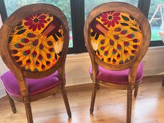 two wooden chairs with painted designs on them sitting in front of a window next to each other