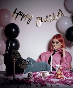 a woman with red hair sitting in front of some balloons and confetti on the floor