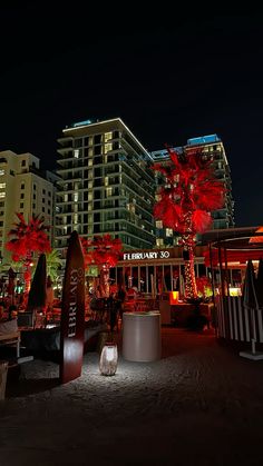 an outdoor restaurant with palm trees lit up in the night sky and people sitting at tables