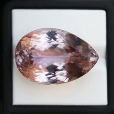 an oval shaped pink diamond sitting on top of a white surface in a black frame