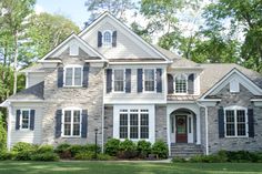 a large gray brick house with white trim and shutters on the front, surrounded by lush green trees