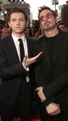 two men standing next to each other in front of a group of people on a red carpet