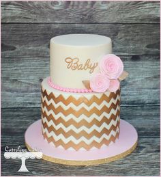 a pink and gold chevroned cake with flowers on the top that says baby