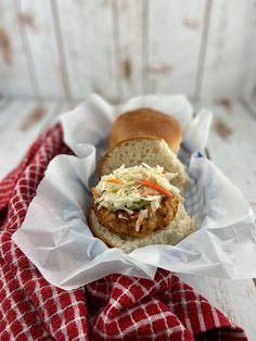 a sandwich with coleslaw in a basket on a red and white checkered cloth