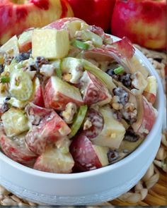 a white bowl filled with fruit salad next to two red and green apples on a woven place mat