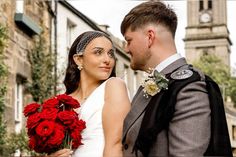 a man and woman standing next to each other in front of a building with red flowers