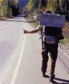 a man walking down the road with a sign on his back that says nowhere in particular