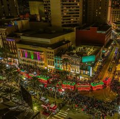 an aerial view of a city street at night with christmas lights on the buildings and people walking around