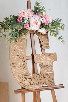 a wooden easel with flowers and greenery on it that has the letter e in cursive writing