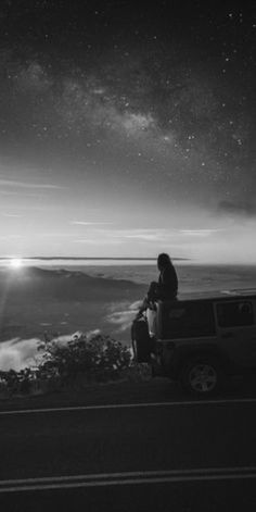 a man sitting on top of a truck next to the ocean under a night sky filled with stars