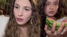 two young women are holding watermelon slices in their hands