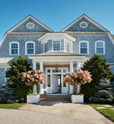 a large blue house with white trim and flowers on the front door, along with two tall trees