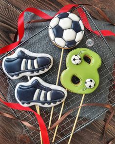 three decorated cookies with soccer themed decorations on top of a wire rack next to a red ribbon