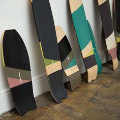 five skateboards lined up against a wall in a row, all painted different colors