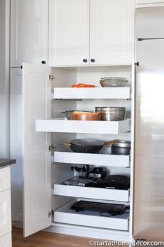 an open refrigerator with pots and pans on it's shelves in a kitchen