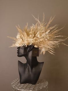 a mannequin's head is adorned with dried grass and feathers for an artistic display