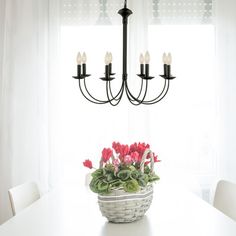 a white table topped with a basket filled with flowers next to a chandelier