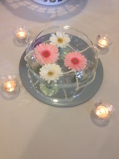 flowers are in a bowl on a table with candles and glass bowls around it for centerpieces