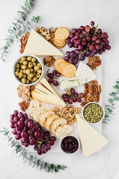 an assortment of cheese, crackers, grapes and nuts on a white platter