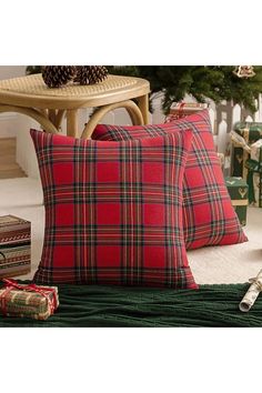 two red and black plaid pillows sitting on top of a green blanket next to a christmas tree