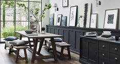 a dining room table with benches and pictures on the wall behind it, in front of a large window