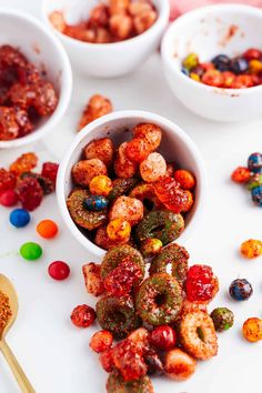 three bowls filled with different colored candies on top of a white surface next to two spoons