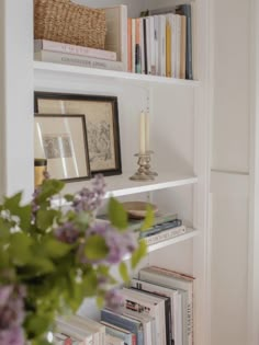 a vase filled with purple flowers sitting on top of a white book shelf next to books