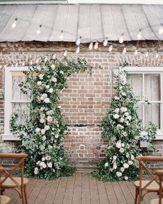 two chairs sitting next to each other in front of a brick building with white flowers