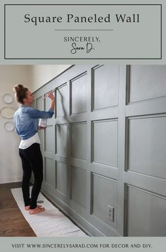 a woman standing on top of a wooden floor next to a gray garage door and painting the doors