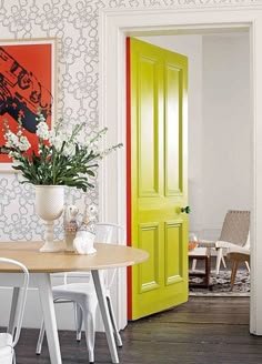 a dining room table with two chairs and a vase on it next to a yellow door