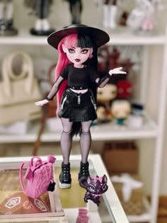 a doll with pink hair wearing a witches hat and black outfit standing on a table