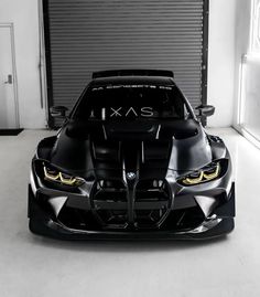 the front end of a black sports car in a garage with an open door behind it