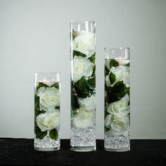 three tall vases filled with white flowers on top of a wooden table next to each other