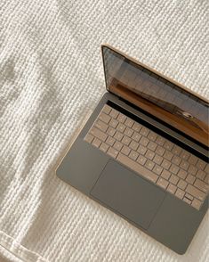 an open laptop computer sitting on top of a white bed cover covered in sheets and pillows