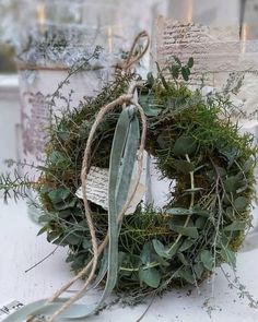 a wreath with some green plants on top of it and two candles in the background