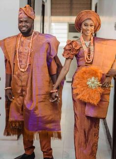 an african couple dressed in orange and purple outfits walking down the hall together with their hands in each others'pockets