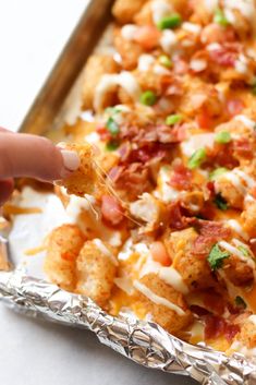 a person dipping some kind of food in to a foil pan with other items on it