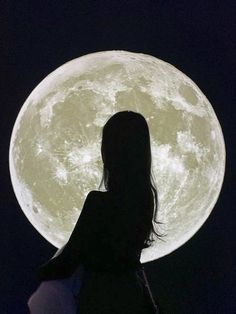 a woman standing in front of the moon with her back to the camera, looking at it