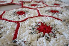 a red and white crocheted blanket with flowers on the center is sitting on a table