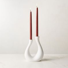 two red candles are in a white vase with one candle sticking out of the side