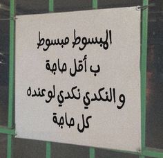 a white sign hanging on the side of a green metal fence with writing in arabic