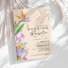 the wedding reception card is next to some palm fronds and other tropical items