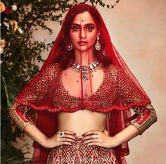 a woman in a red bridal outfit with jewelry on her head and hands on her hips