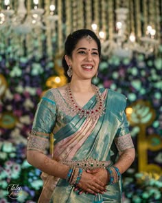 a woman in a green sari smiles at the camera while standing next to a chandelier