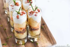 small glasses filled with desserts sitting on top of a wooden cutting board and topped with green garnish