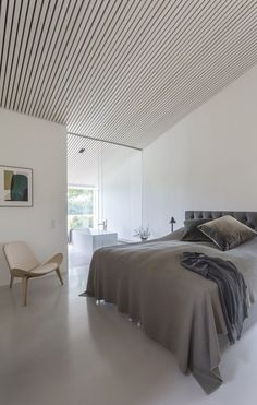 a bedroom with white walls and flooring has a bed, chair, and artwork on the wall